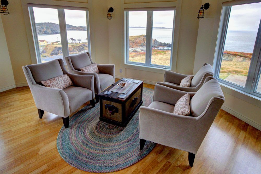 Lichte woonkamer met vier fauteuils, een houten salontafel en grote ramen met uitzicht op het water.