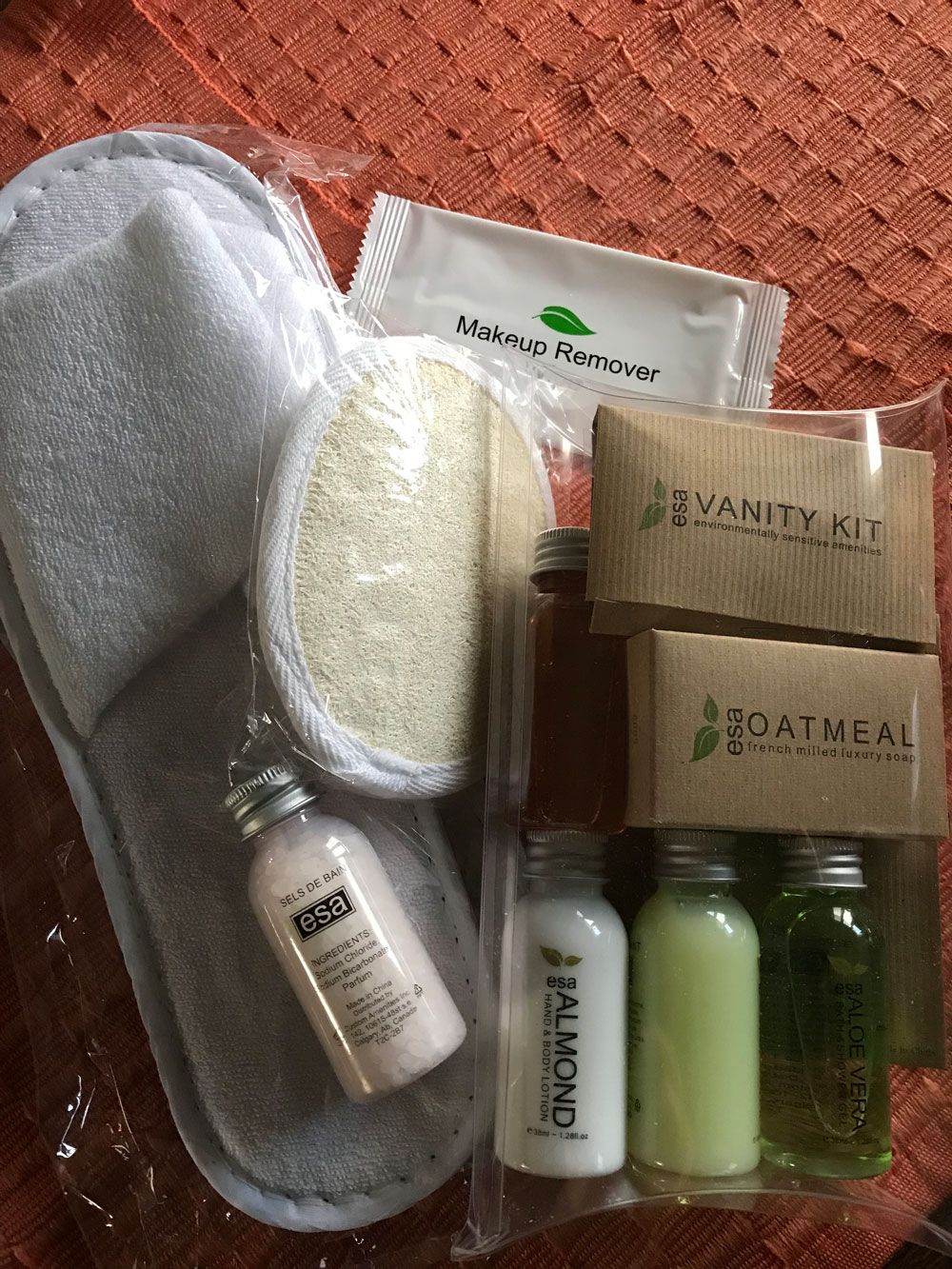 Spaset met handdoek, spons, lotion, zeep en kleine flesjes, uitgestald op een rood, patroonrijk oppervlak.