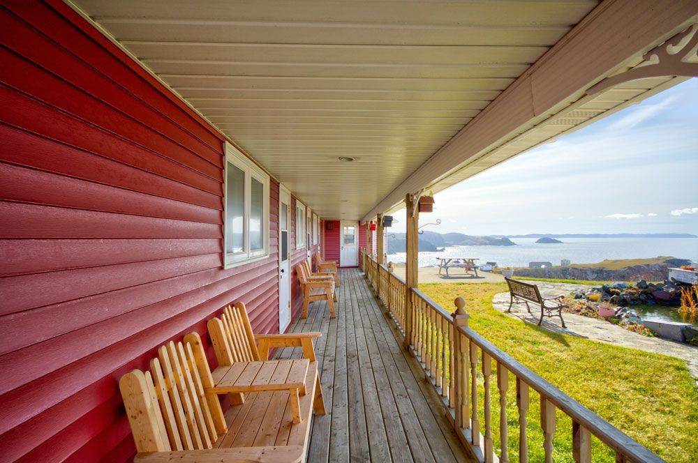 Veranda van een rood huis met houten stoelen, met uitzicht op een grasveld en de oceaan.