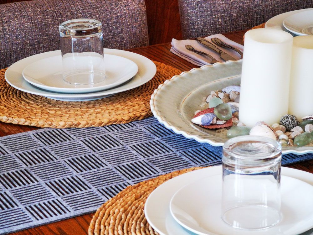 Dek de tafel met witte borden, glazen, kaarsen, schelpen en geweven placemats op een tafelloper met een patroon.