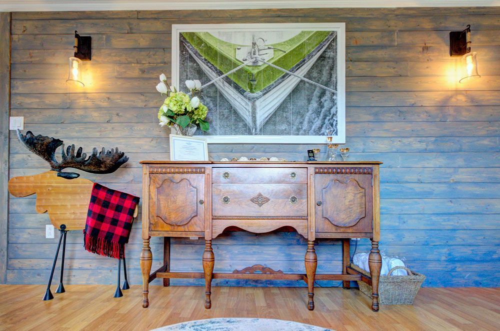 Rustieke consoletafel met wanddecoratie, wandlampen, bloemen en een rood geruite plaid in een kamer met houten lambrisering.
