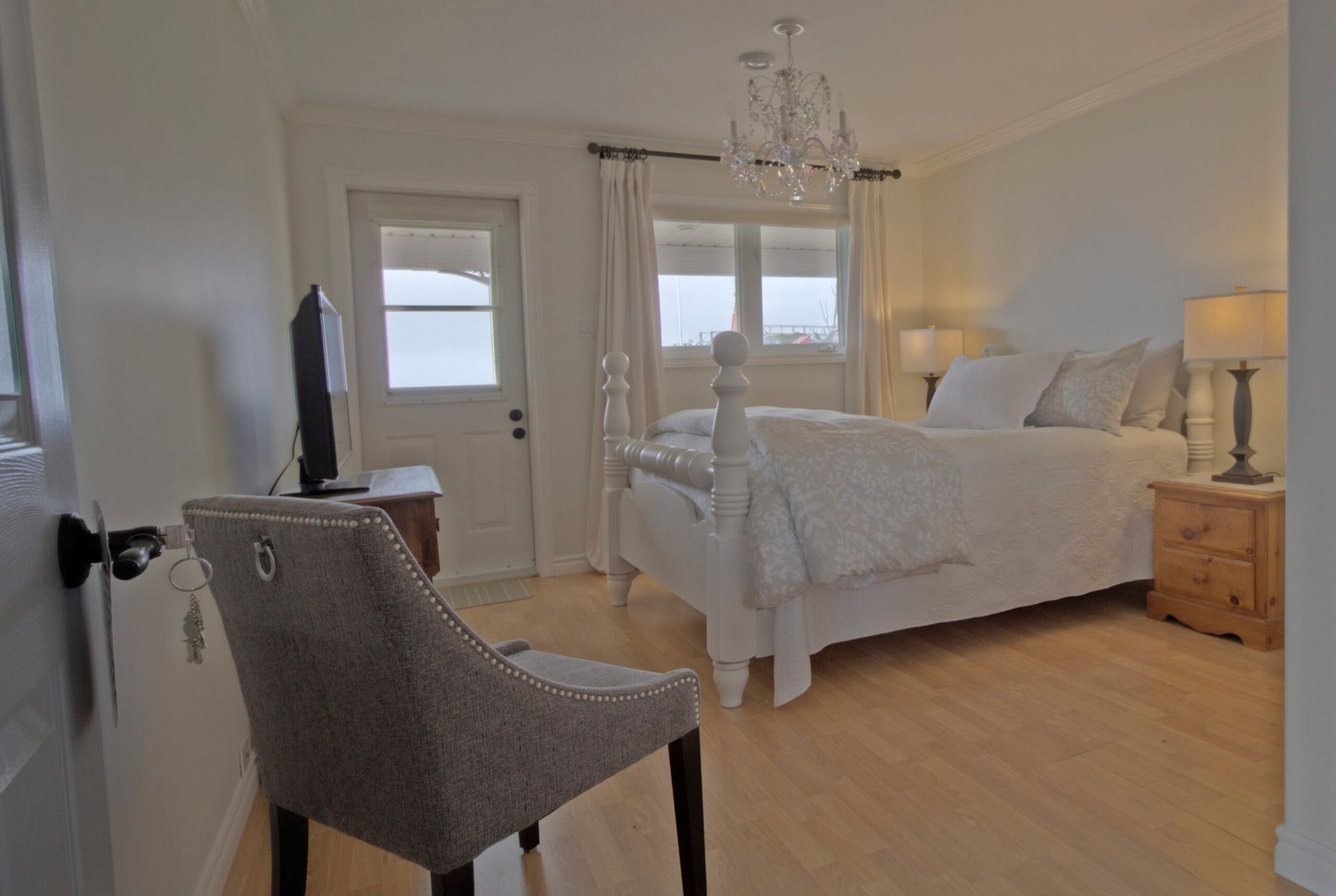 Lichte slaapkamer met wit bed, grijze stoel, houten nachtkastje en lichte houten vloer.