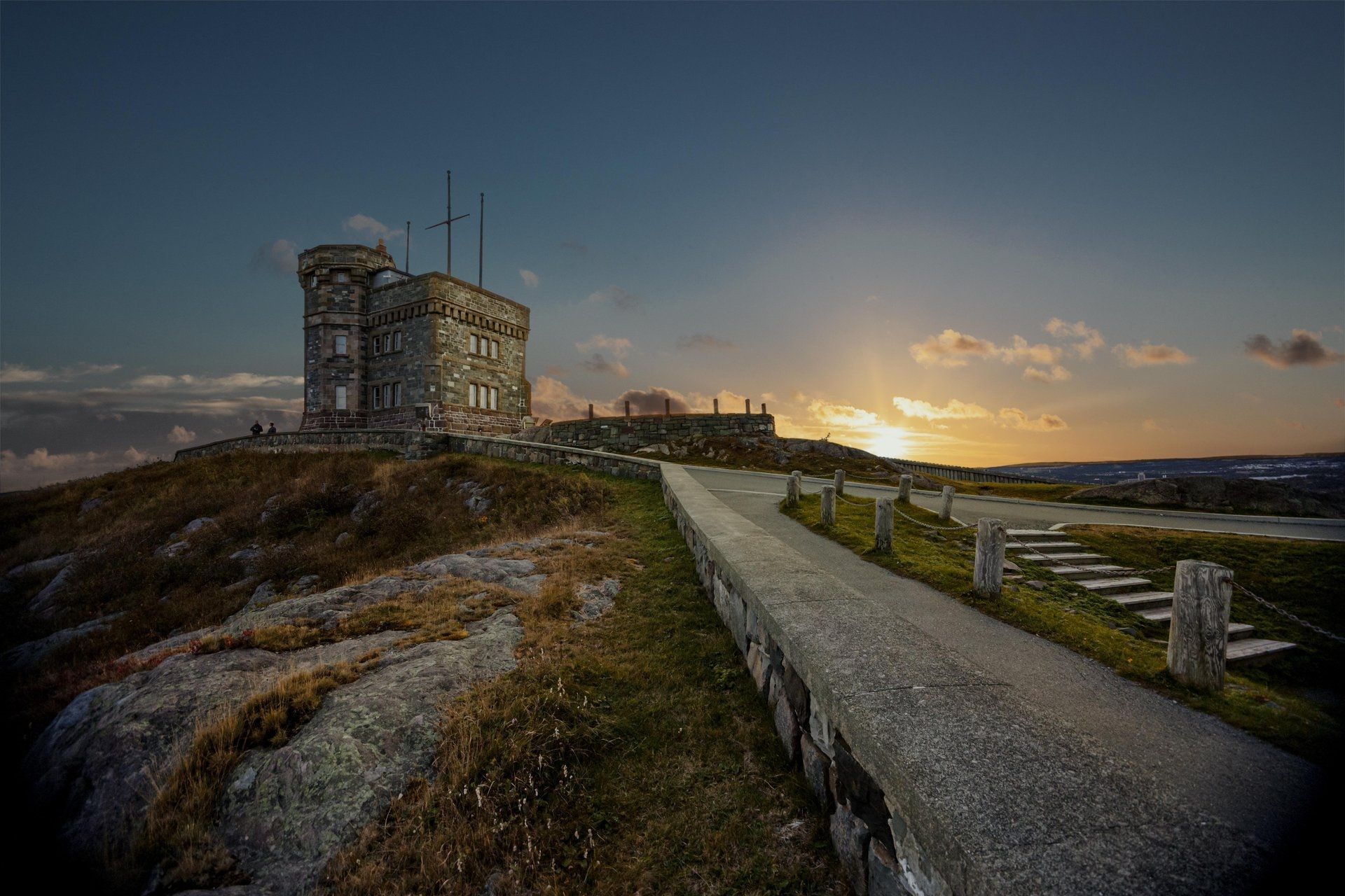 Stenen uitkijktoren Cabot Tower op Signal Hill te St. John's Canada langs een kronkelend pad bij zonsondergang met uitzicht over een kustlandschap.