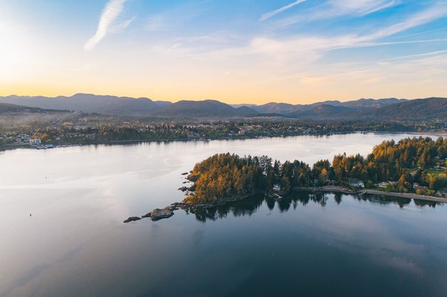 Luchtfoto van een kalm meer bij zonsondergang met een bebost eiland en bergen in de verte.