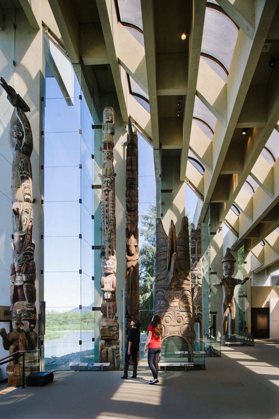 @Destination Canada Interieurbeeld van een museum met diverse totempalen in de tentoonstelling. Twee personen staan bij een centrale paal.