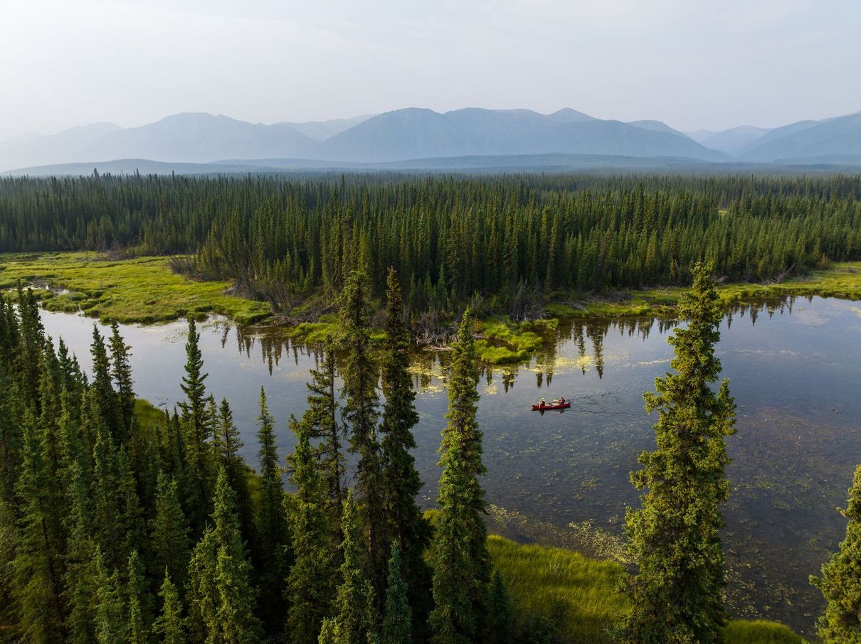 Prachtige rivier in West Canada Luchtfoto van een beboste riviervallei met bergen in de verte en twee kano's op het water.