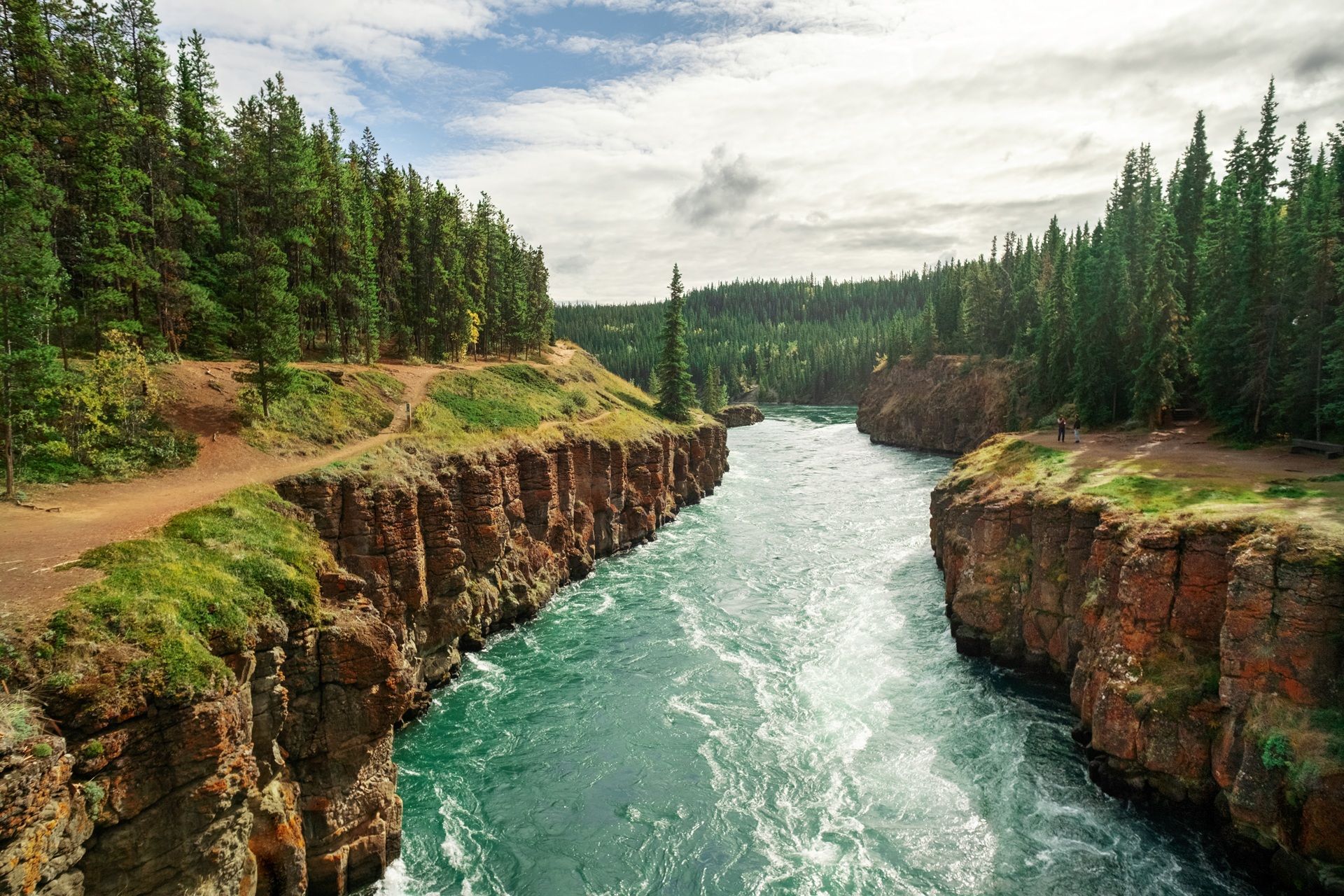 @ Destination Canada A turquoise river flows through a canyon lined with reddish-brown rock and evergreen trees.