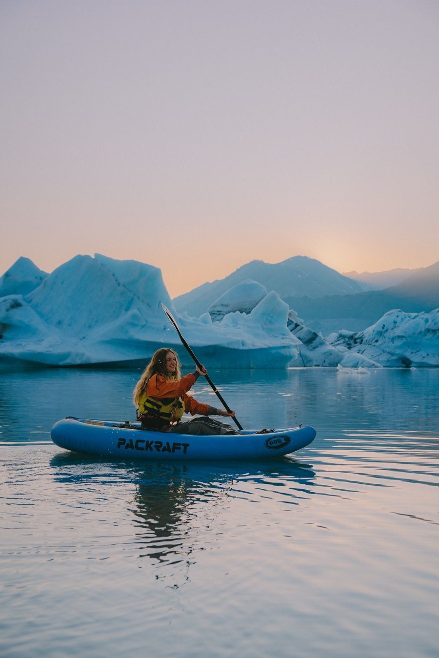 @danimarielister IG@danimarielisterDanielle Lister Woman kayaking among icebergs in a blue lake, holding a paddle; sunset in the background.