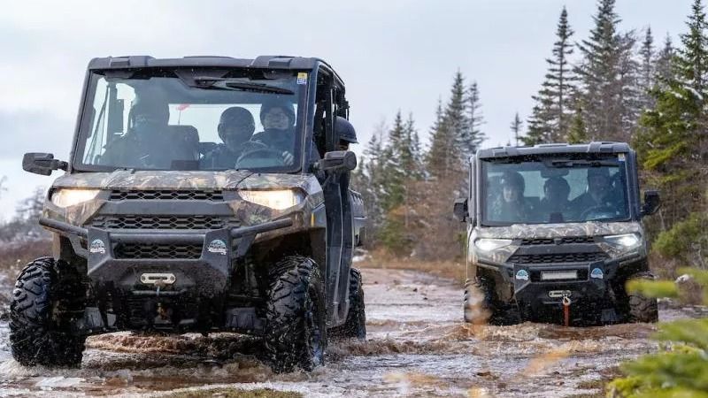 Twee terreinwagens rijden door een modderig, besneeuwd bospad.
