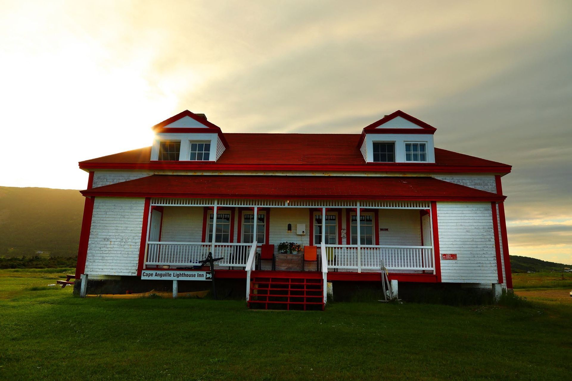 Rode boerderij met een witte veranda en een rood dak bij zonsondergang op een grasveld.