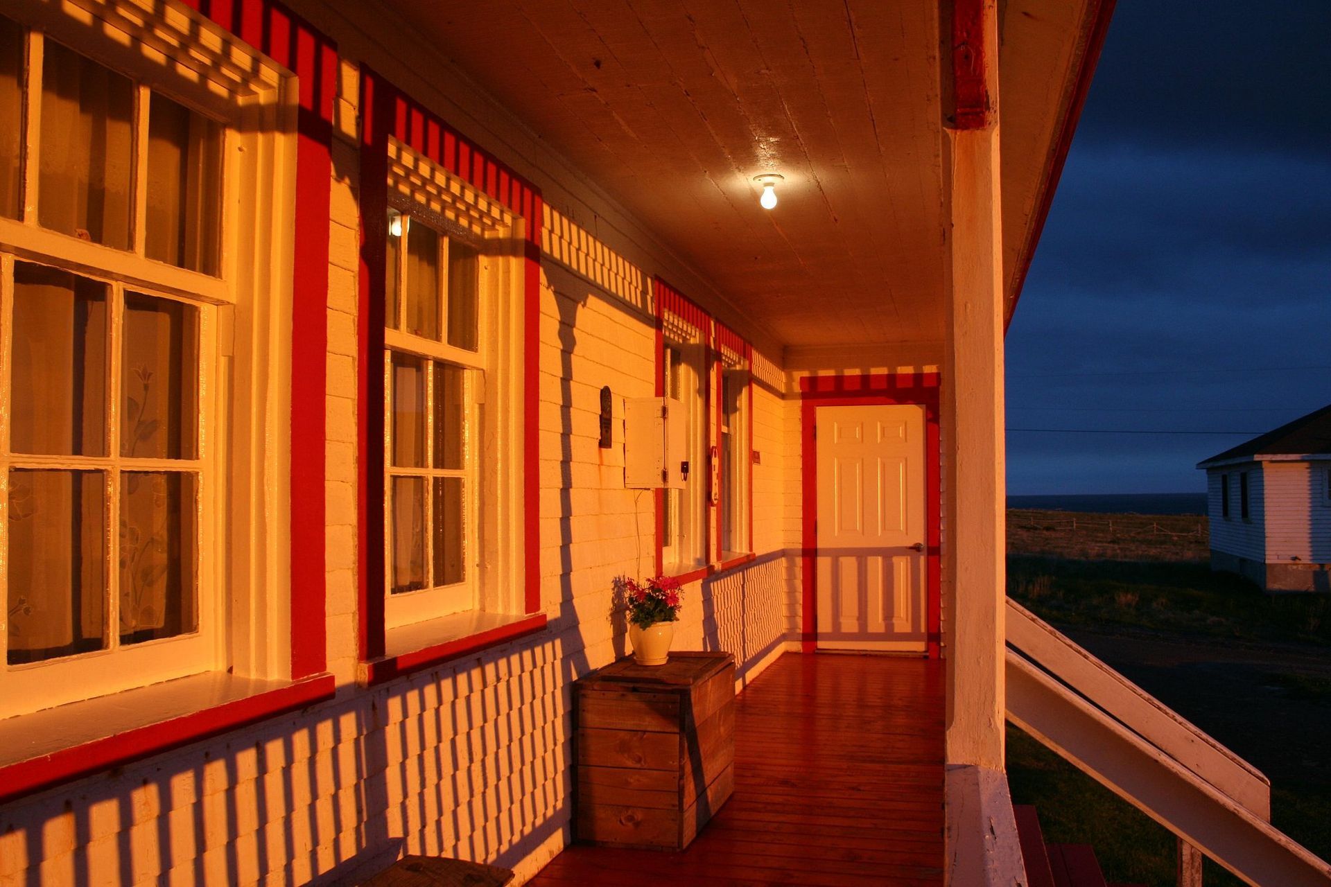 Veranda met zonsonderganglicht, witte balustrade, houten vloer en uitzicht op de oceaan.