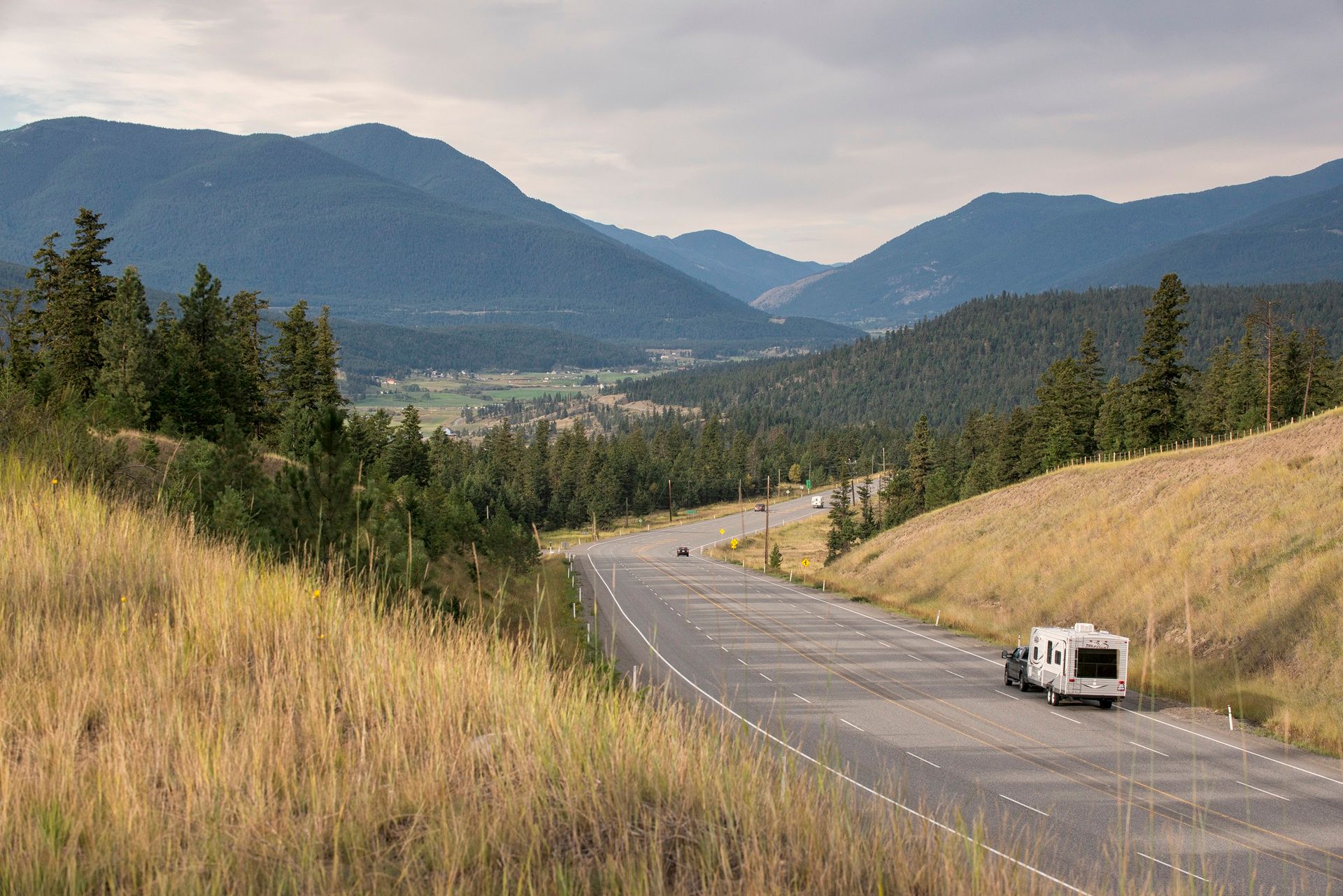 De Cariboo Highway in Canada met een camper die door droge graslanden en met dennenbomen bedekte heuvels rijdt.