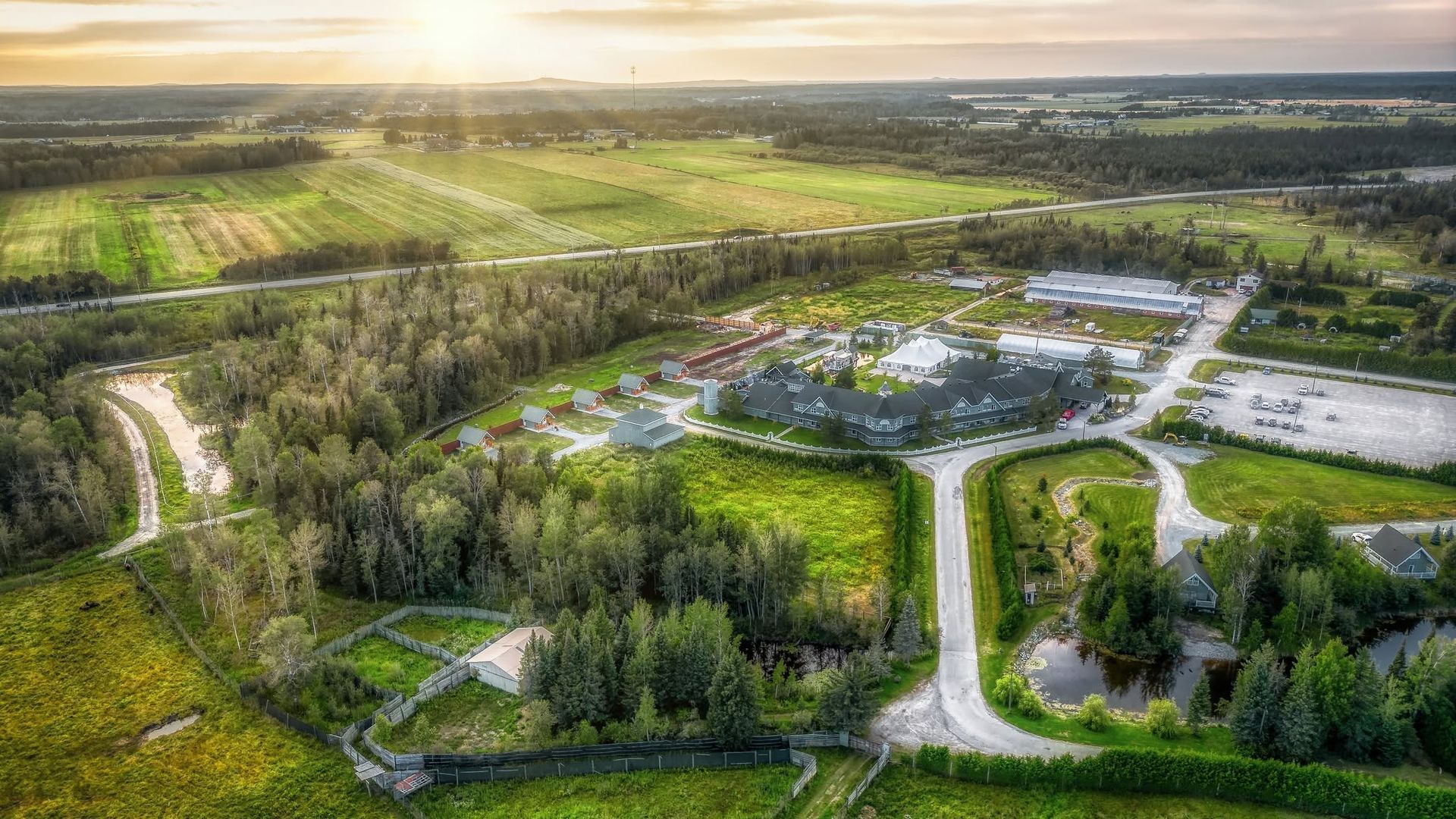 Luchtfoto van het hoofdgebouw van Cedar Meadow met wegen, bomen en velden bij zonsondergang.
