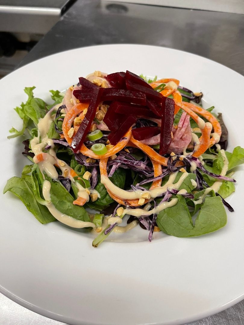 Kleurrijke gemengde salade met bladgroenten, bieten, wortels en romige dressing op een wit bord.