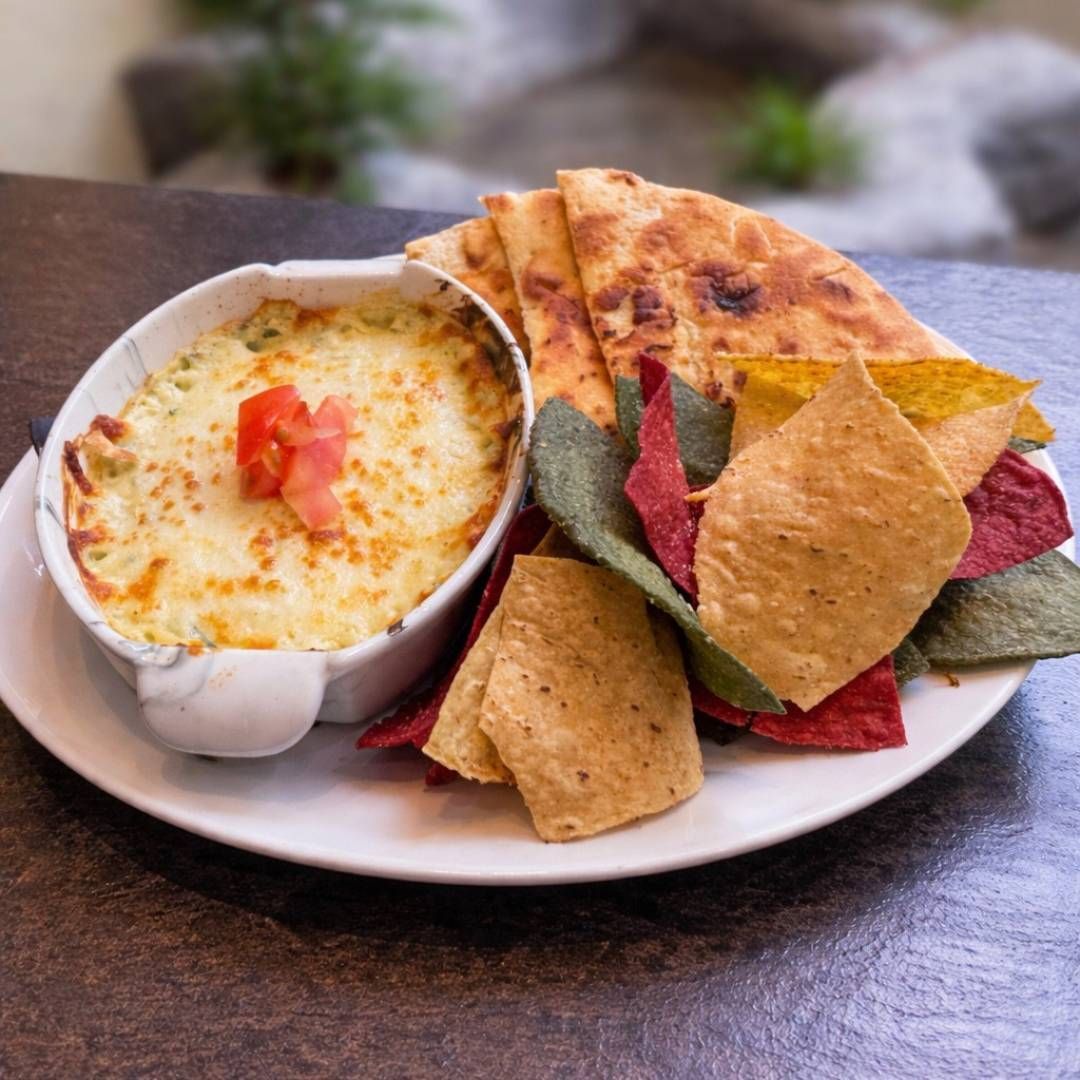Gebakken kaasdip met tortillachips en platbrood op een wit bord, buiten geserveerd.