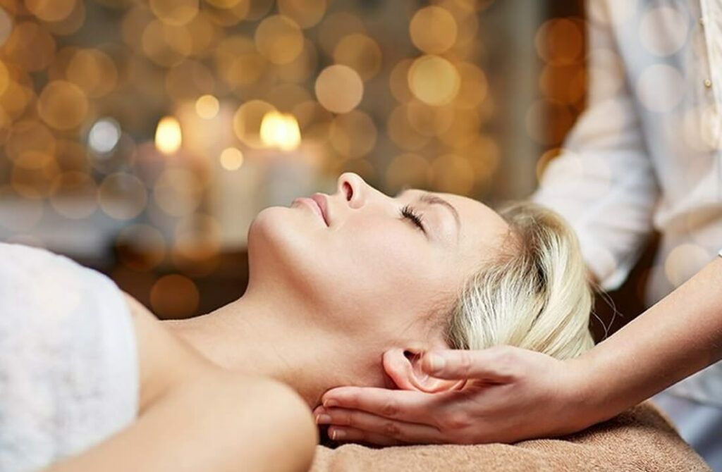 Vrouw krijgt een hoofdmassage in een spa, met warme, wazige lichten op de achtergrond.