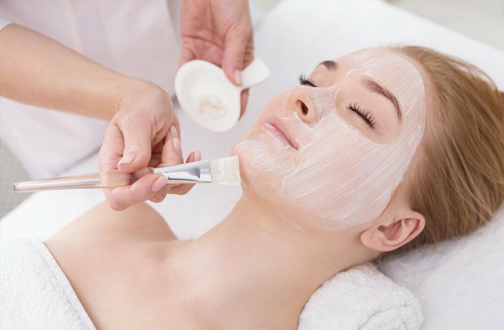 Gezichtsbehandeling waarbij crème op het gezicht van de klant wordt aangebracht in een spa-omgeving.