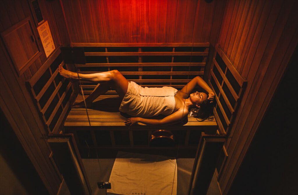 Een persoon ligt op een bed in een smalle, warm verlichte houten kamer met rood-oranje verlichting.