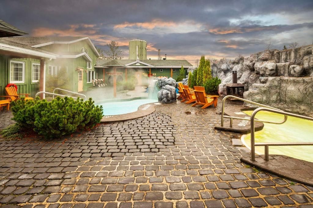 Een geplaveid terras met zwembad, oranje stoelen en een stenen huis onder een bewolkte hemel.