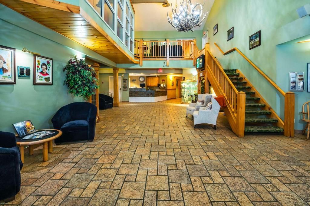 Ruime hotellobby met tegelvloer, houten trap, balkon, banken en kroonluchterverlichting.