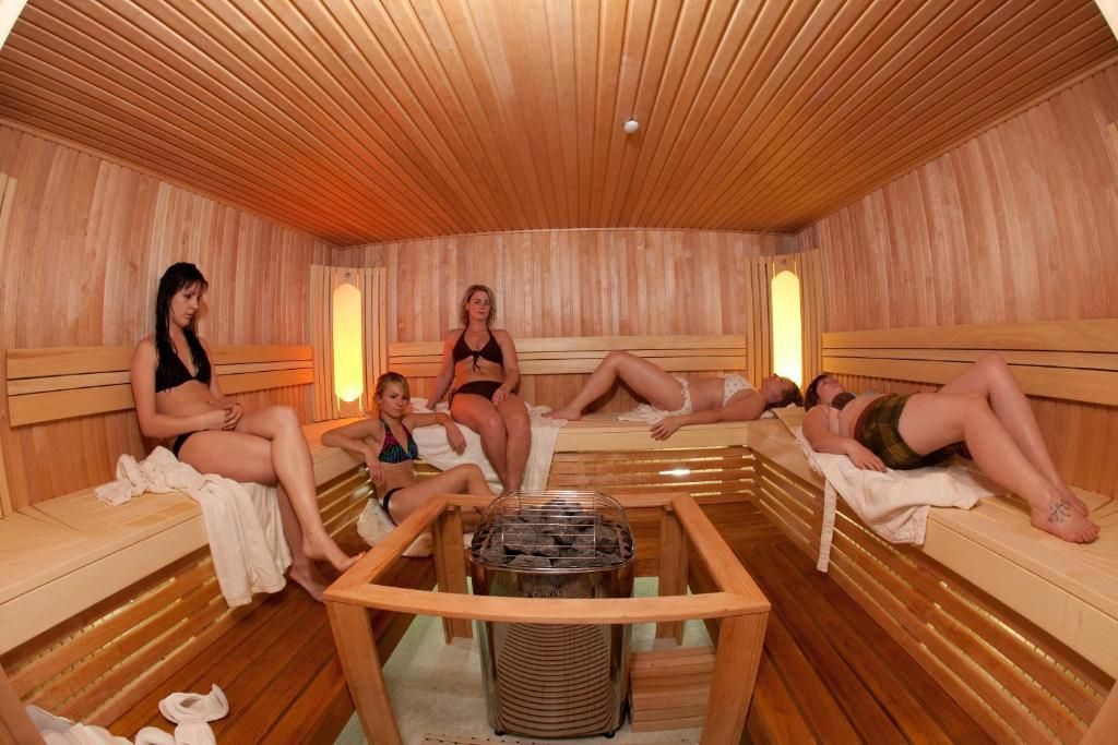 Mensen ontspannen in een sauna met houten lambrisering, centrale verwarming en warme oranje verlichting.