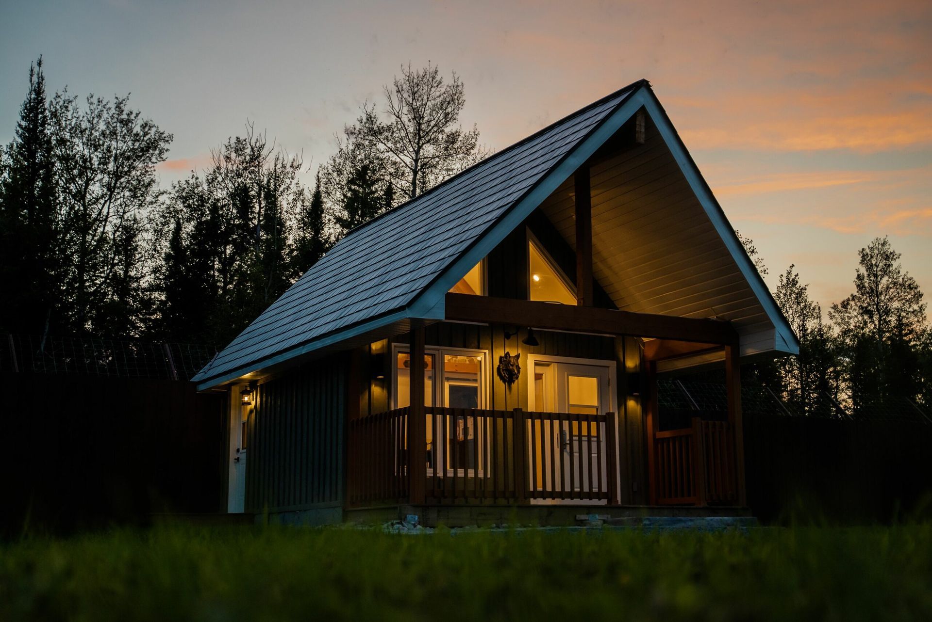 Gezellige houten hut van Cedar Meadow met warm licht dat in de schemering gloeit, omgeven door donkere bomen en gras.