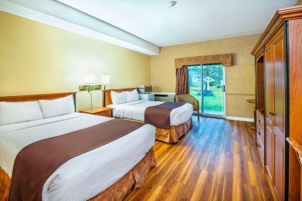 Lichte hotelkamer van Cedar Meadow met twee bedden, houten vloer, een kledingkast en openslaande deuren naar het groen.
