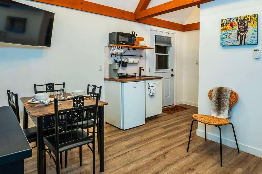 Kleine eethoek met een aan de muur gemonteerde tv, een kitchenette en twee gevlochten stoelen op een houten vloer.