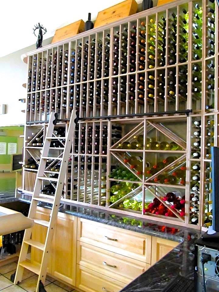 Een wand met wijnrekken vol flessen, met een ladder voor een houten kast.