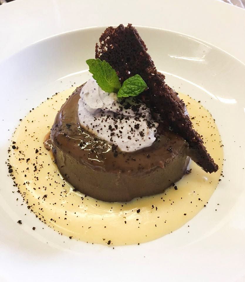 Chocoladedessert met slagroom, munt en kruimelgarnering op een wit bord.
