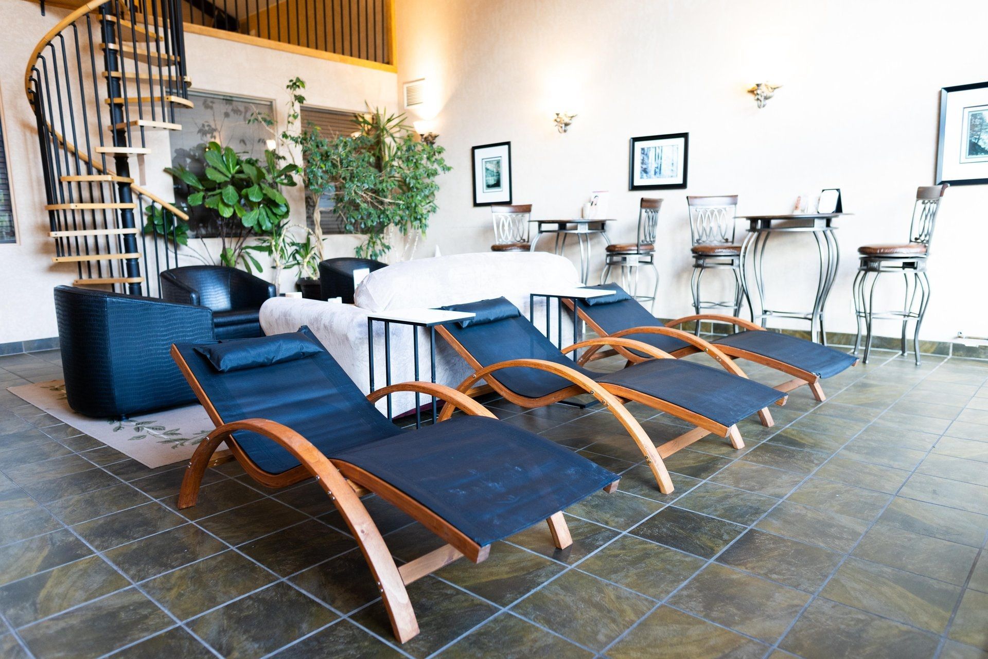 Moderne lounge met donkerblauwe chaise longues, witte tafels en potplanten op een stenen vloer.
