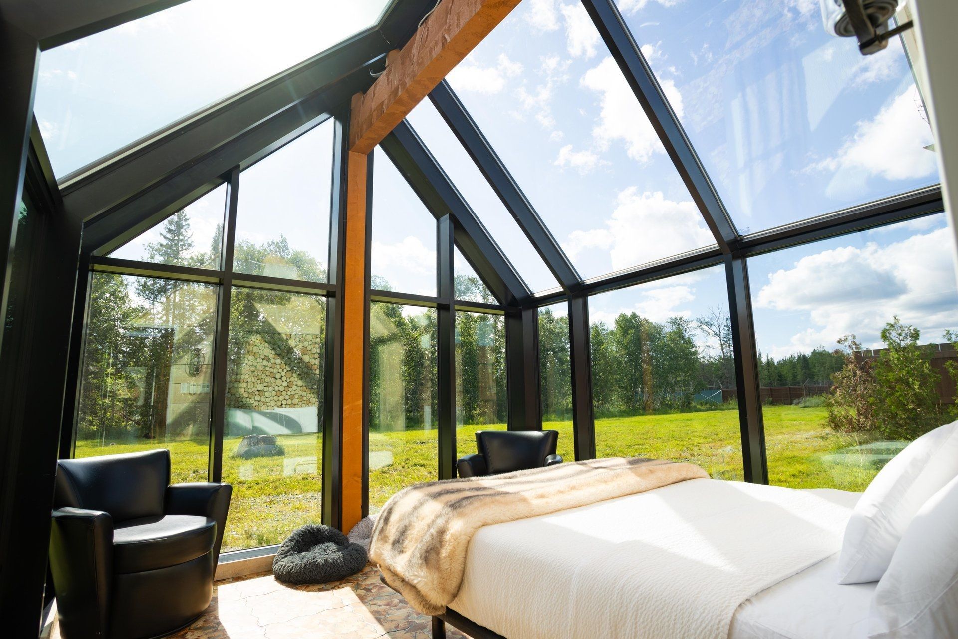 Moderne slaapkamer met glazen wanden, een bed en zwarte stoelen, met uitzicht op een groen veld.