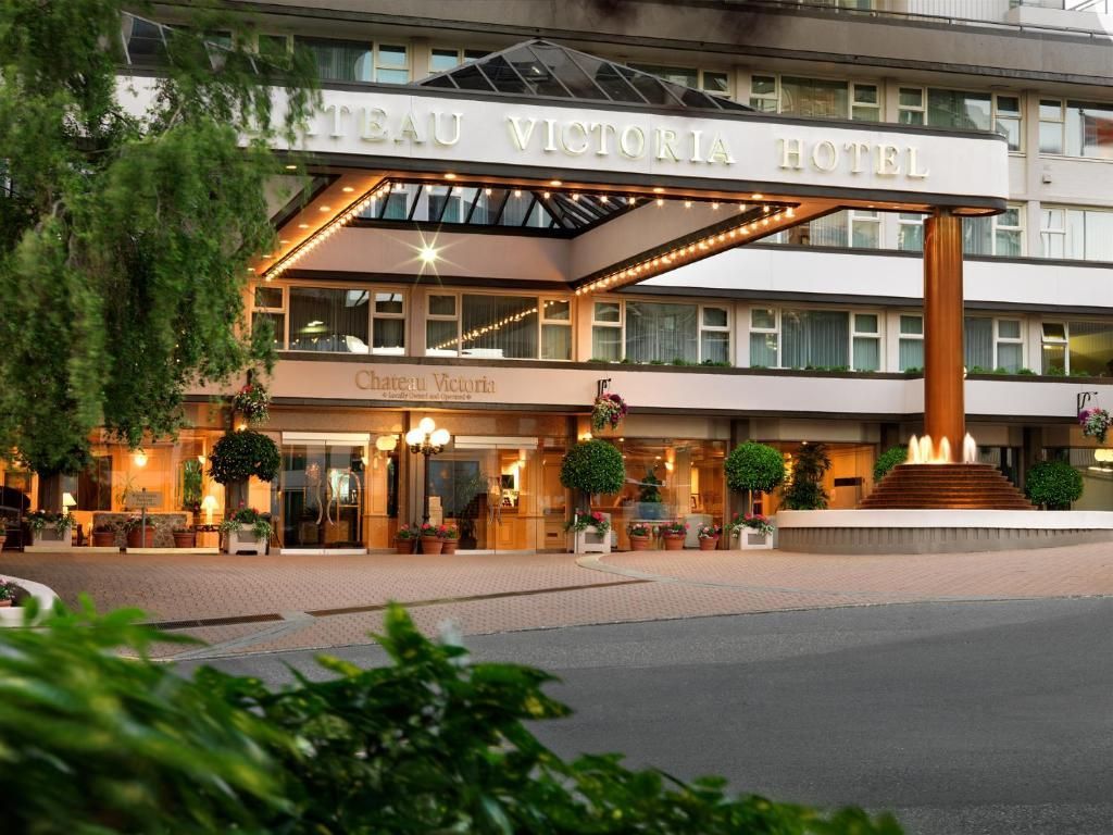 Ingang van het Victoria Hotel met verlichte luifel, potplanten en uitzicht op de straat bij schemering.