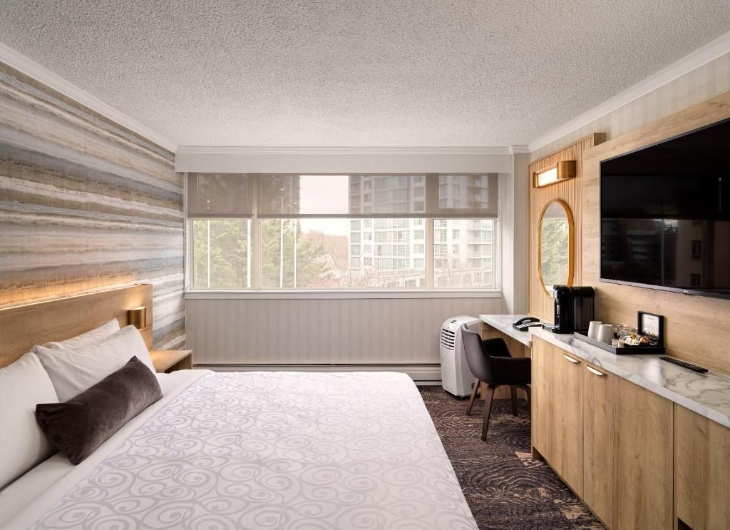 Moderne hotelkamer met bed, bureau, tv aan de muur en groot raam.