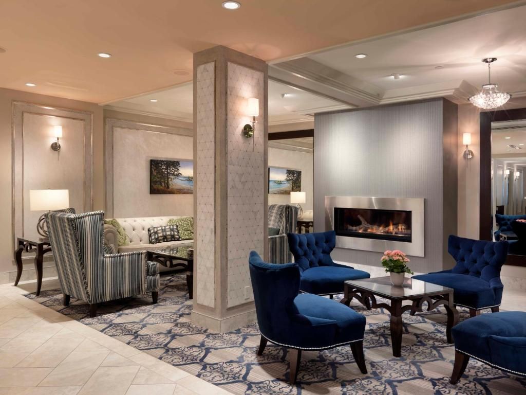 Elegante hotellobby met blauwe stoelen, een bank met patroon en een brandende open haard onder zacht inbouwlicht.