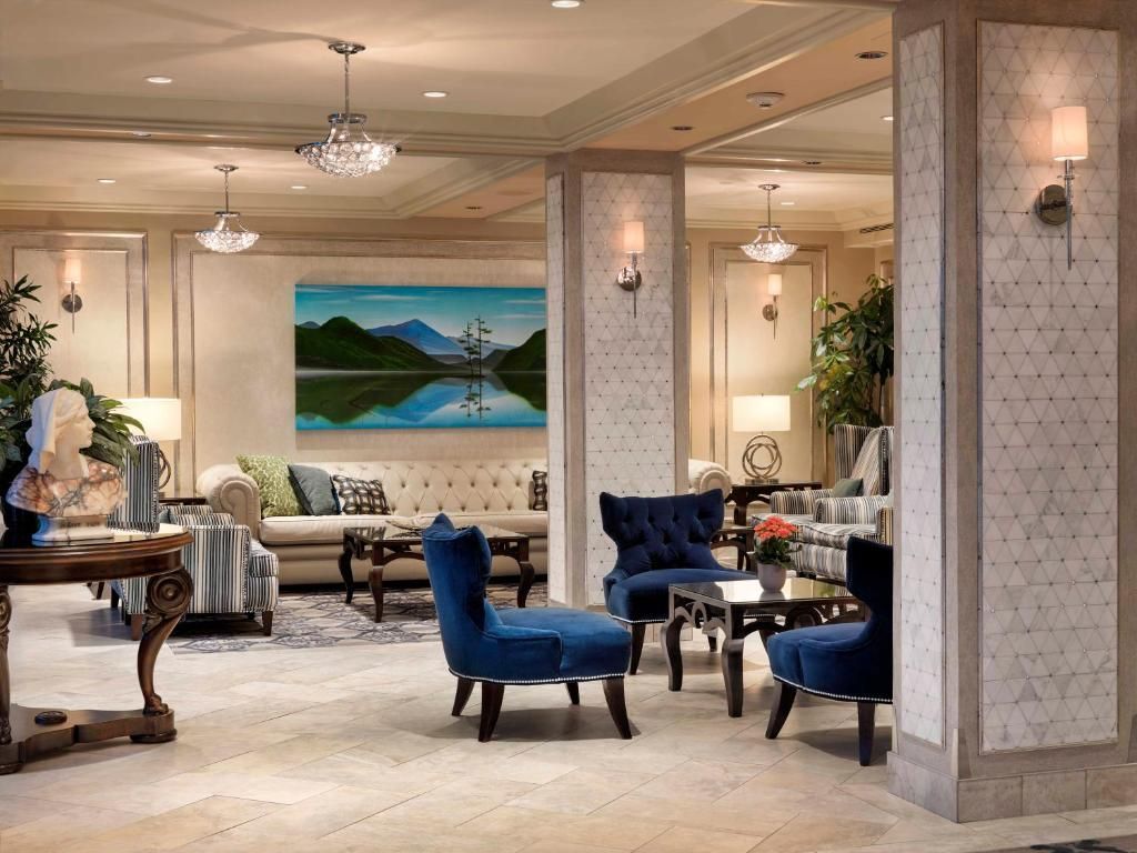 Elegante hotellobby met blauwe stoelen, kroonluchters en een groot landschapsschilderij.