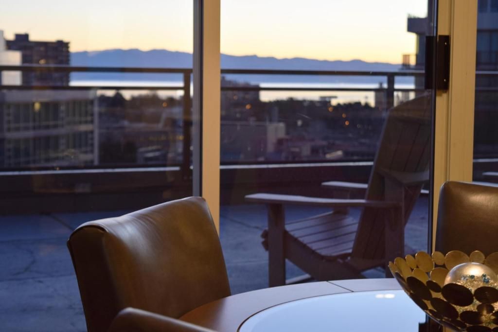 Hotellounge met leren fauteuils en een tafel met uitzicht op de skyline van de stad bij zonsondergang.