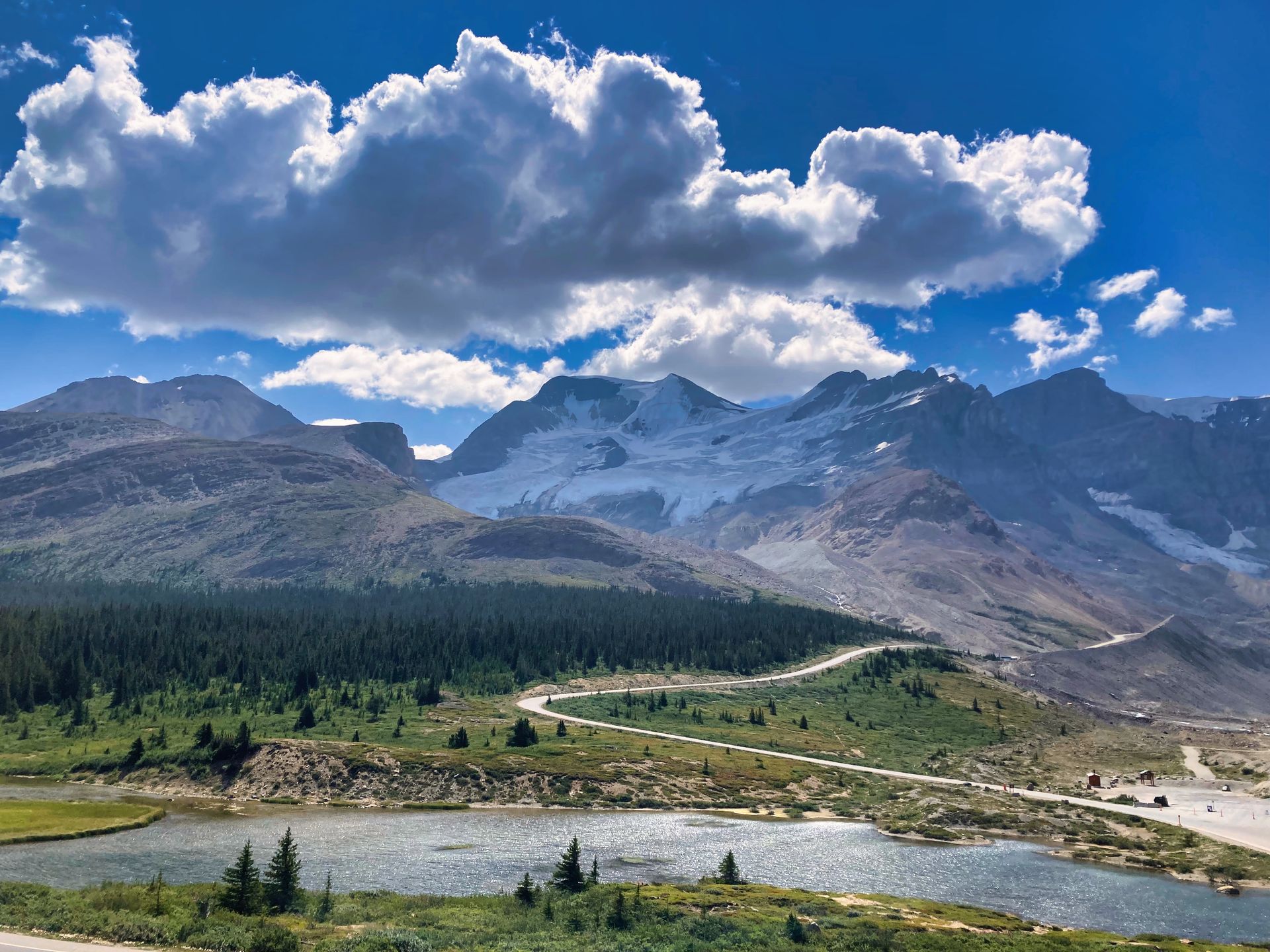 De Icefields Parkway met een kronkelende rivier, een groene vallei en dramatische wolken boven rotsachtige bergtoppen.