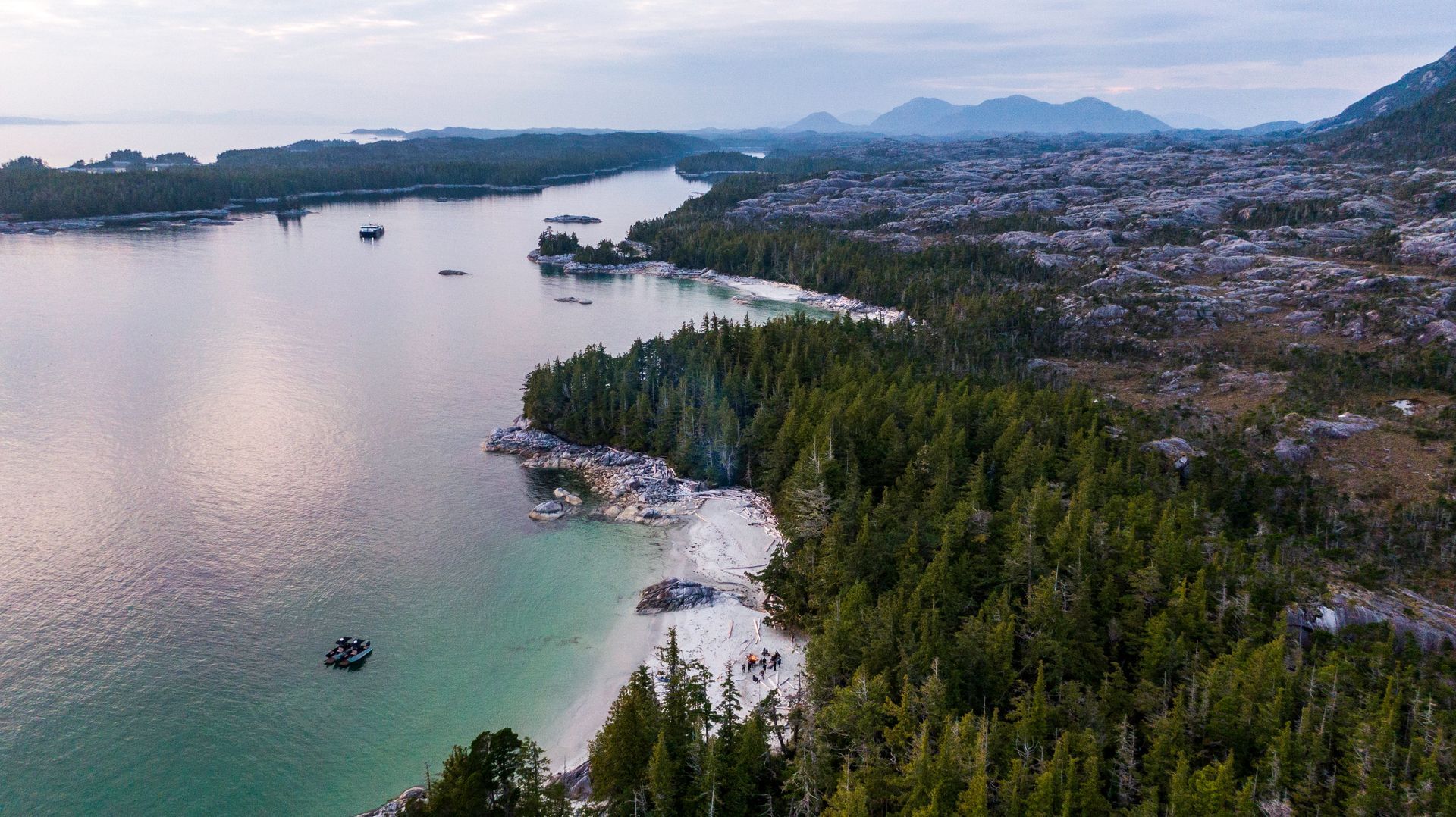 Kustbaai in British Columbia met turquoise water, groene kustlijn, het schip de Cascadia van Maple Leaf Adventures en bergen in de verte bij zonsondergang