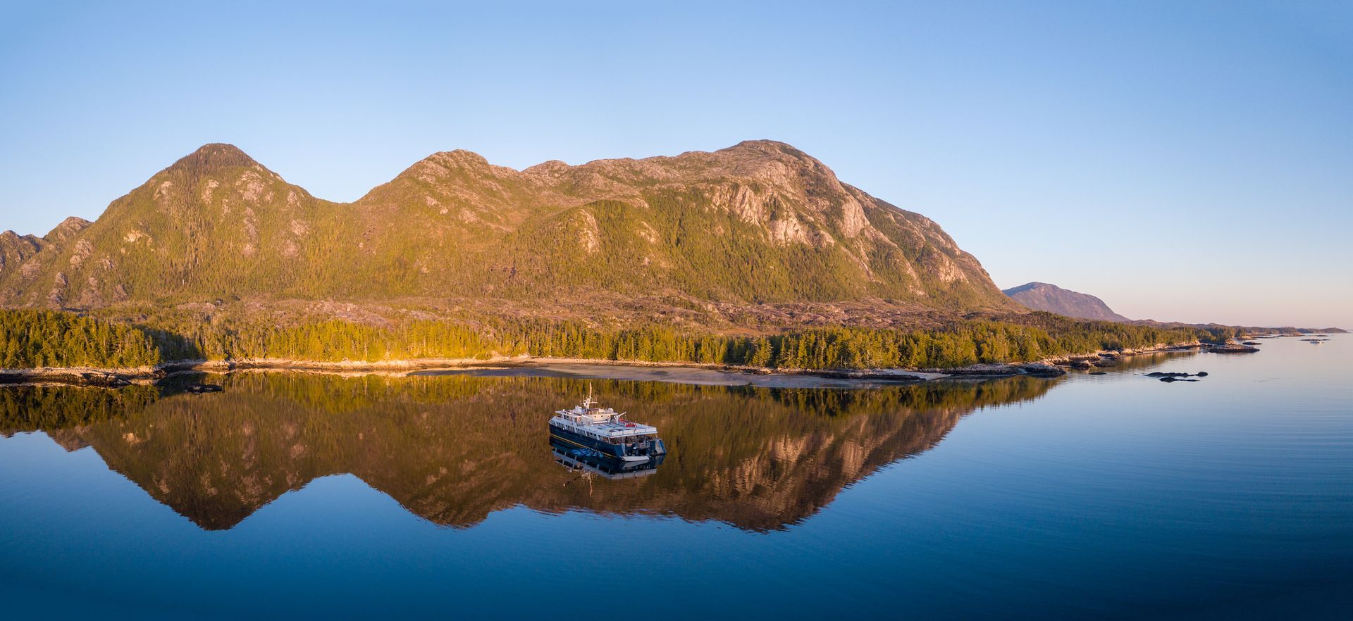 Een berg weerspiegeld in een kalm meer, met het schip Cascadia van Maple Leaf Adventures bij zonsondergang in British Columbia