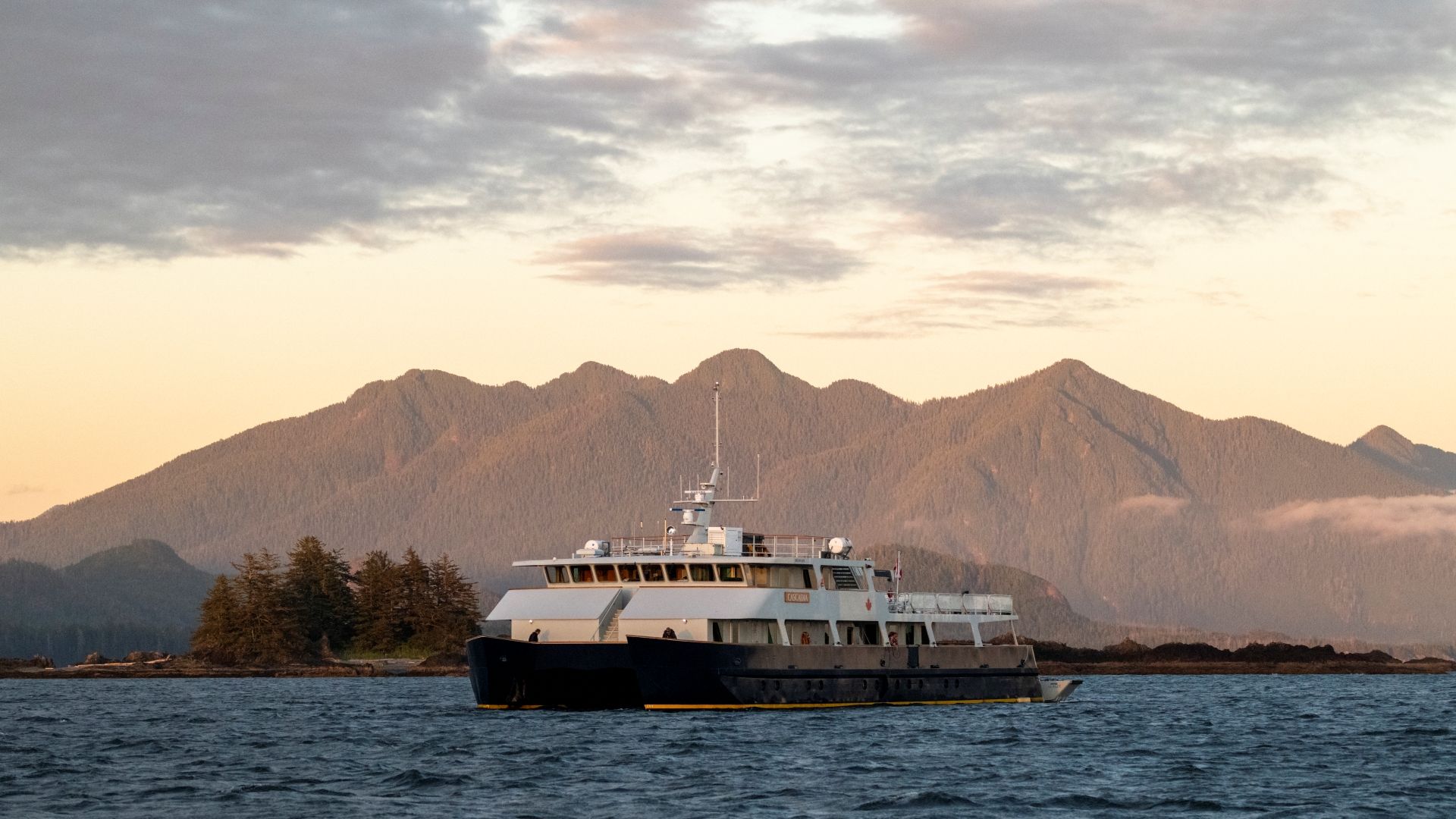 Het schip Cascadia van Maple Leaf Adventures op kalm water met bergen op de achtergrond bij zonsondergang