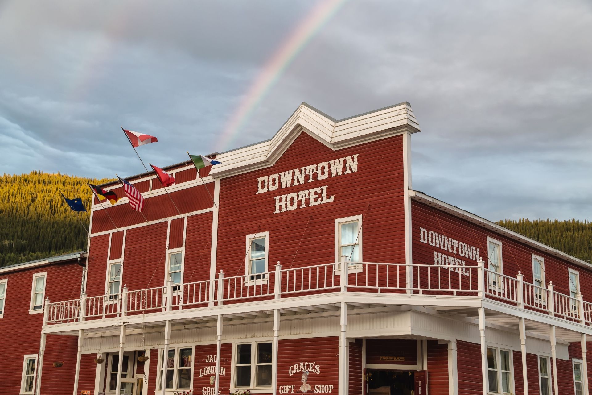 © Rhonda Krause Rood hotel in het centrum van Dawson City, Yukon, met witte accenten onder een regenboog in een bergdorp.