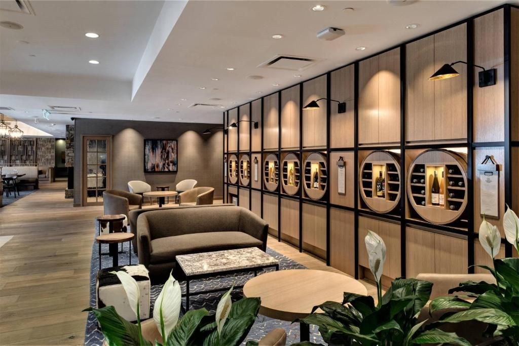 Moderne hotellounge met banken, tafels, planten en een glazen wand die de zithoek afschermt.