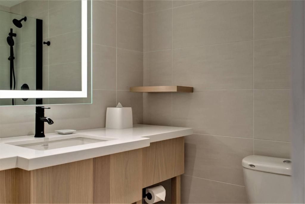 Moderne beige badkamer met houten wastafelmeubel, wit aanrechtblad, spiegel en zwarte kraan.