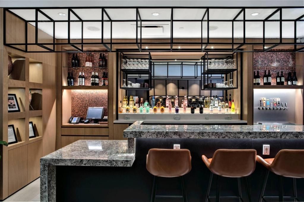 Modern barinterieur met marmeren toonbanken, houten planken, flessen en sfeervolle hanglampen.