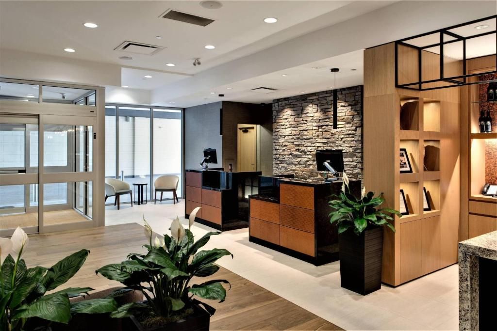 Moderne kantoorlobby met houten receptiebalie, potplanten en glazen toegangsdeuren.