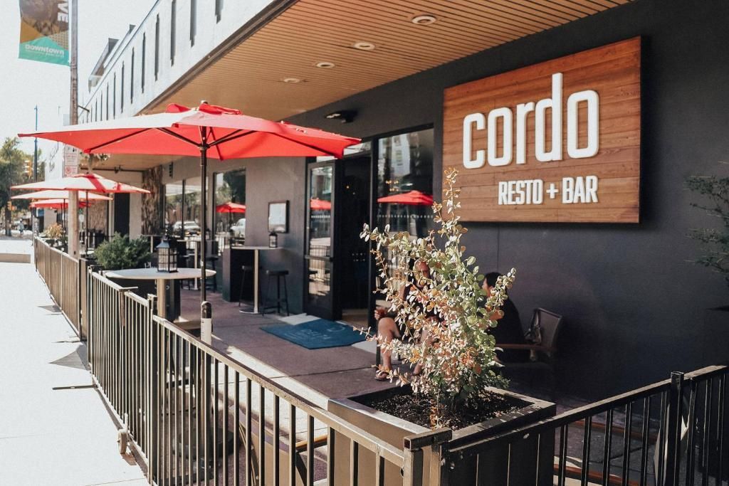 Buitenterras van Cordo Resto + Bar met rode parasols en een zwarte balustrade naast een modern gebouw