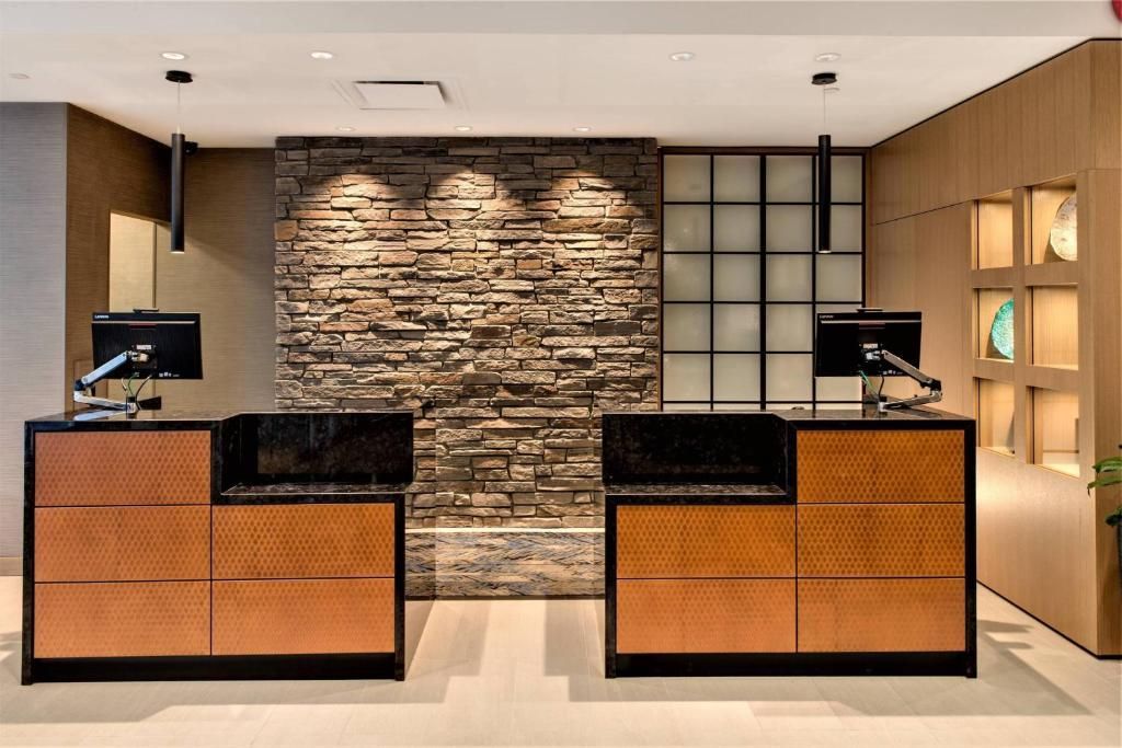 Moderne hotelreceptie met twee zwarte en houten balies tegen een accentmuur van natuursteen.