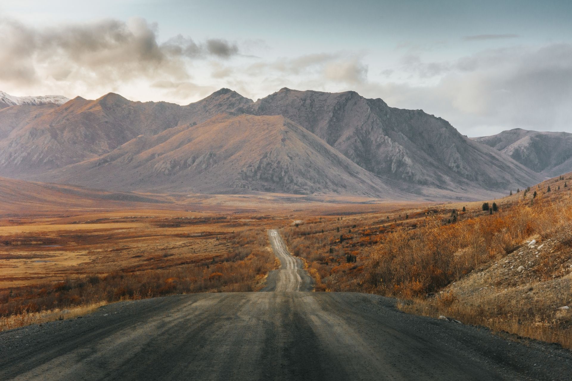 @victoraerden Dempster Highway door een kale vallei in Yukon, richting ruige bergen onder een bewolkte hemel.