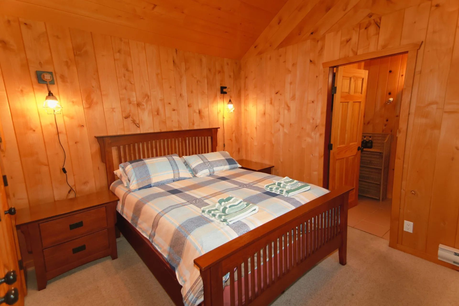 Gezellige slaapkamer met houten lambrisering, een houten bed, een houten nachtkastje en een open deur naar de gang.
